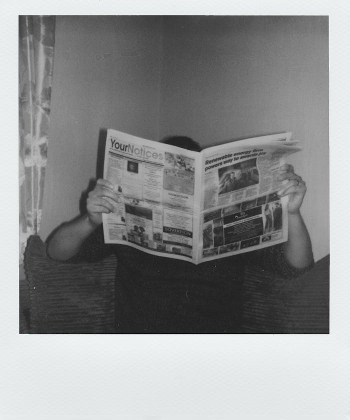 Person reading a newspaper at home in a vintage black and white style.
